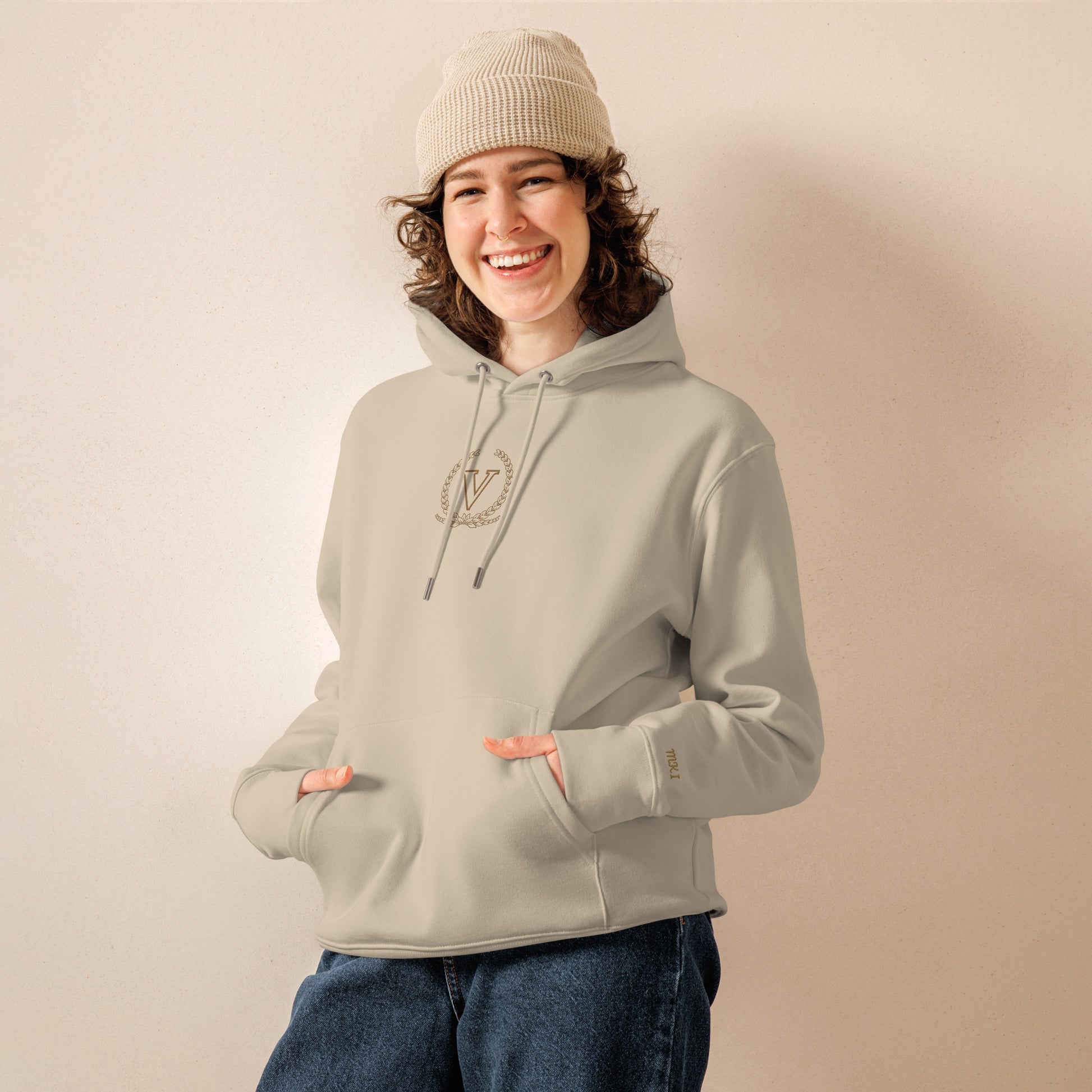 Person wearing a light gray hoodie and beige beanie on a plain background